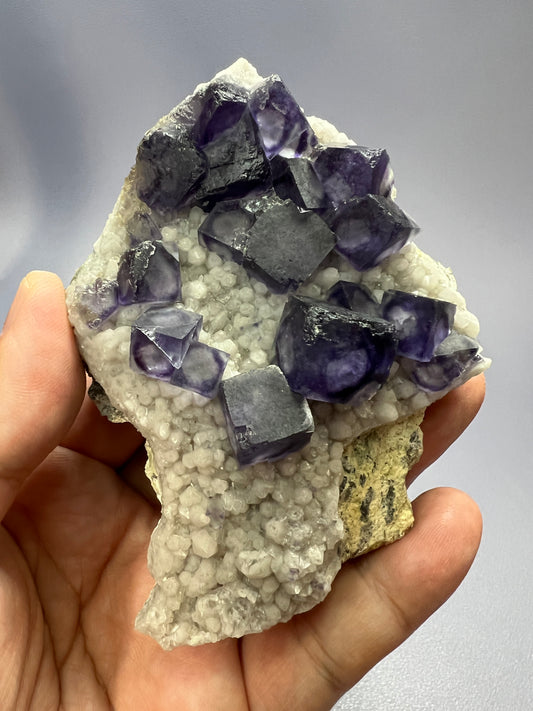 a hand holding a piece of purple and white rock